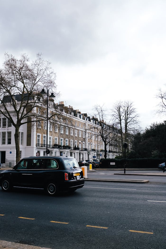 A quintessential London street scene featuring a black taxi cab, classic buildings, and overcast skies.