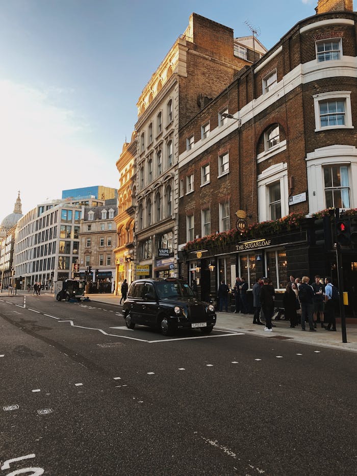 A bustling London street scene featuring classic architecture, a black taxi, and people enjoying an evening out.